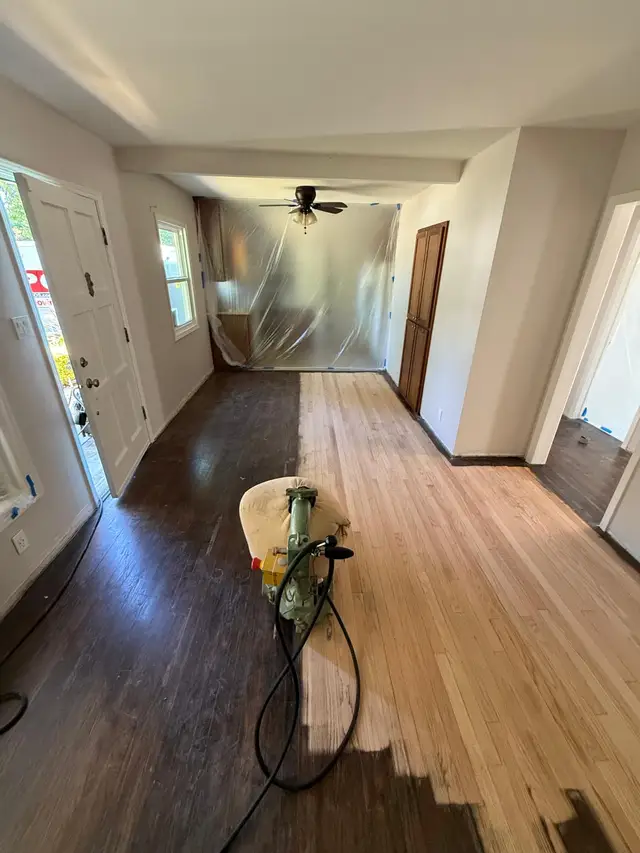 Hardwood floor refinishing in progress, drum sander revealing bare oak next to old dark finish